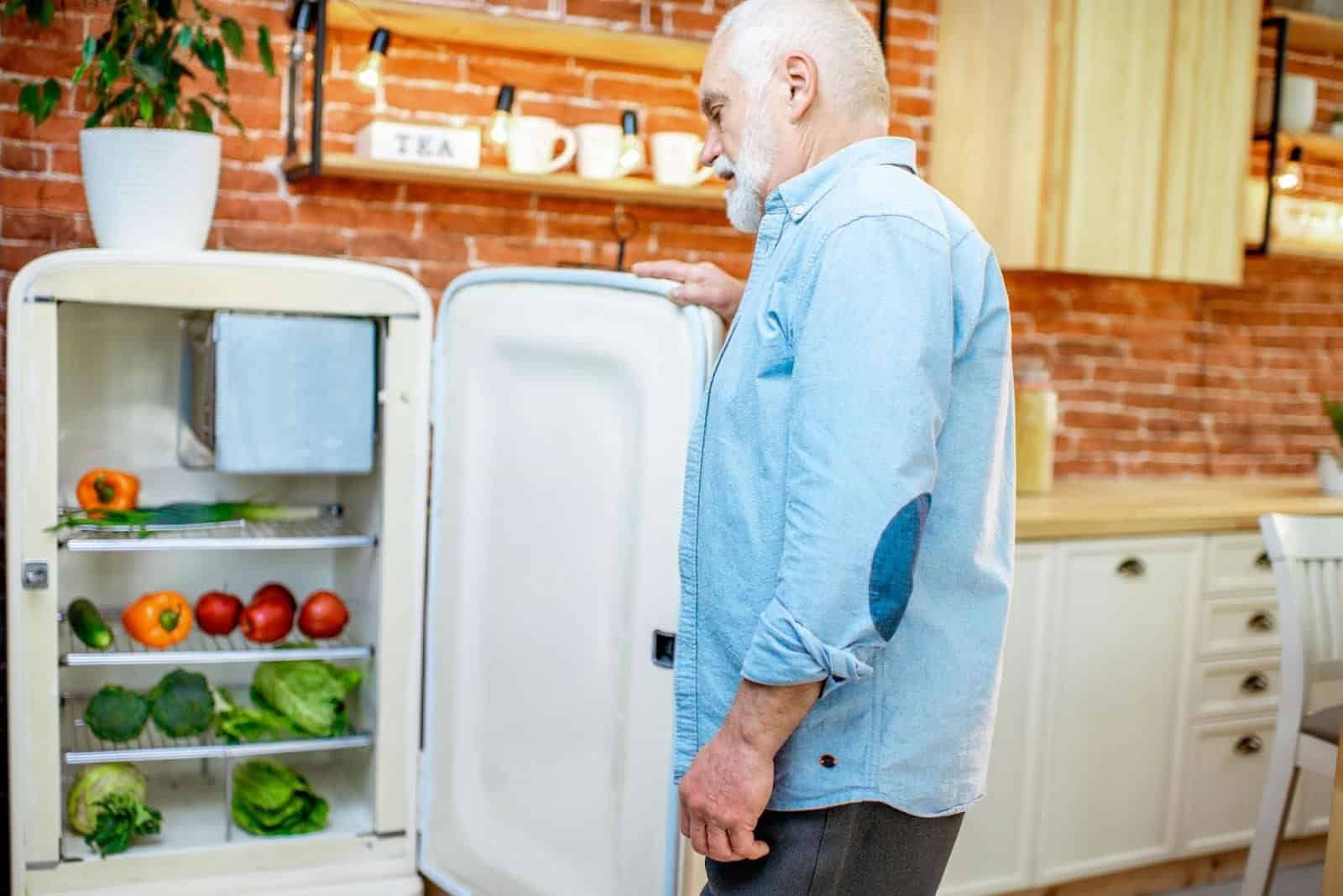 Older man inspecting the inside of his refrigerator, checking the freshness of stored vegetables.